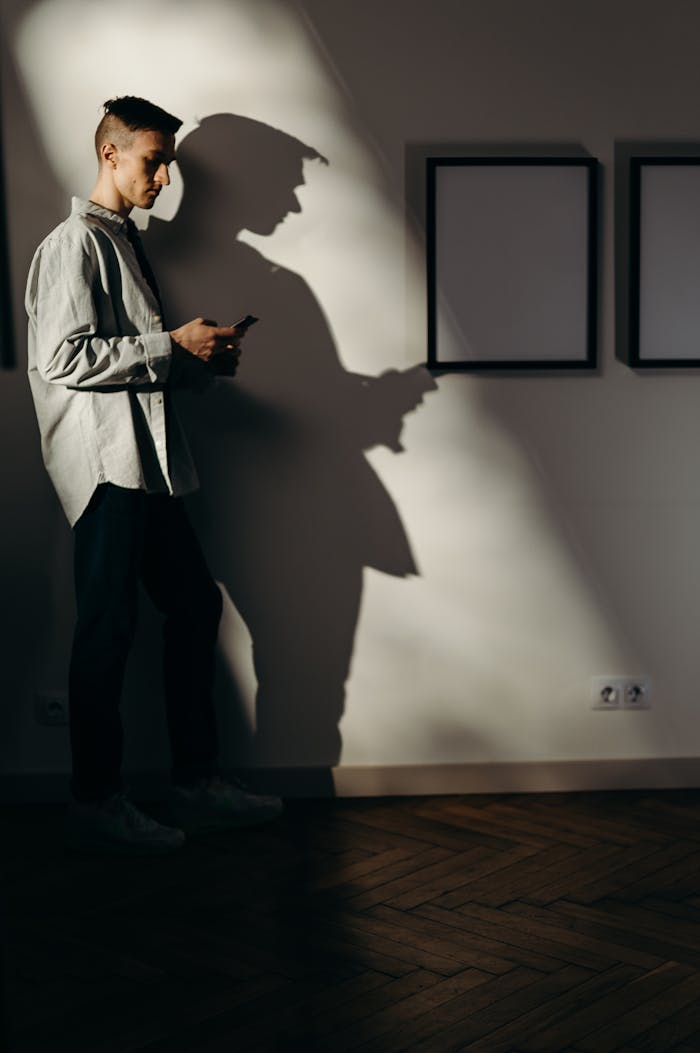 An adult man with smartphone in a minimalist art gallery, casting a shadow.
