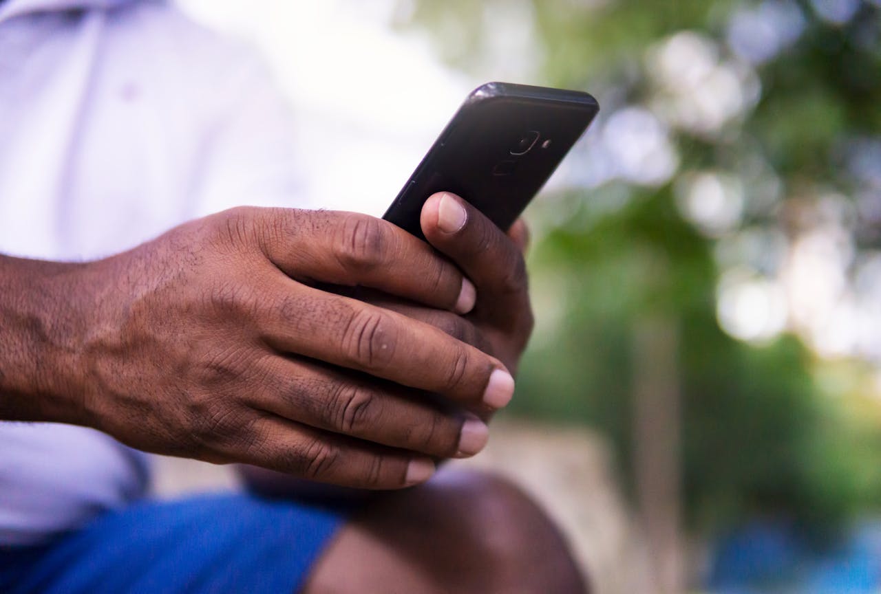 A close-up of a mans hands holding a smartphone in a park setting, showcasing technology use.