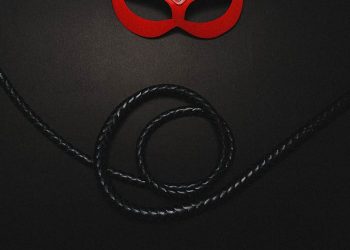A red leather mask paired with a black whip, evoking themes of mystery and sensuality.